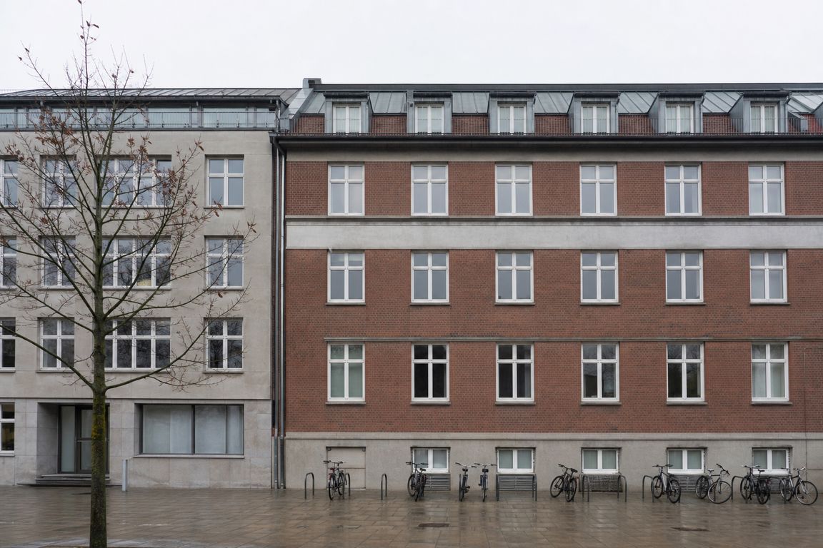 Die Backsteinfassade eines gewöhnlichen norddeutschen Bürogebäudes an einem breiten Gehweg, davor abgestellte Fahrräder bei bedecktem Himmel