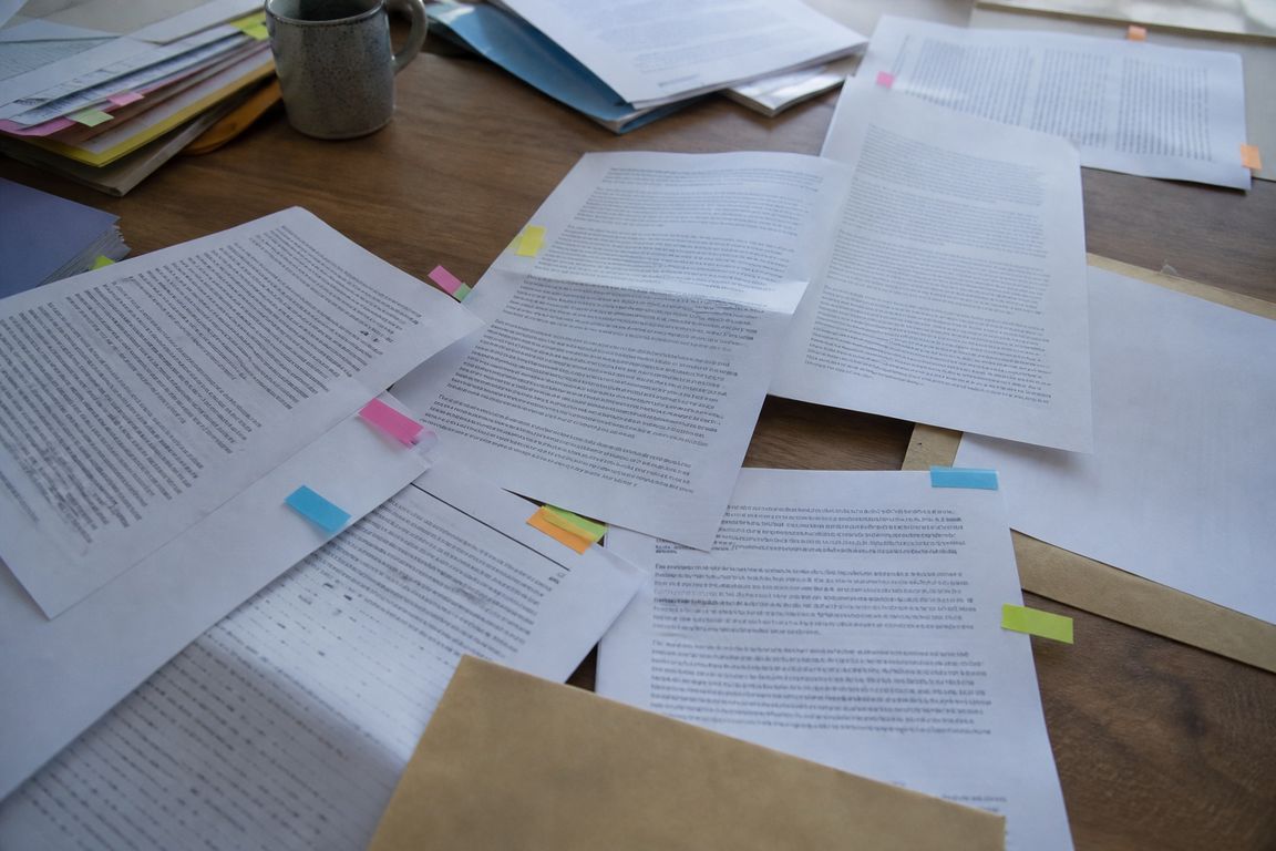 Mehrere aufgeschlagene Briefe und Ausdrucke liegen ausgebreitet auf einem Tisch, an ihren Rändern kleben bunte Haftmarker