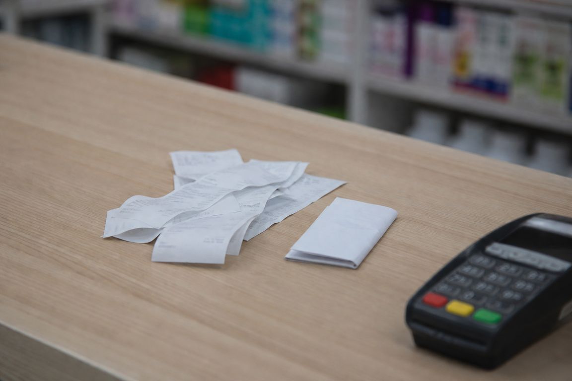 Ein kleiner Stapel schmaler Kassenbelege und ein zusammengefalteter Verordnungsbeleg auf einem hellen Apothekentresen
